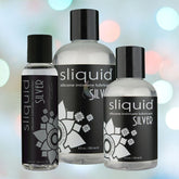 Three bottles of Sliquid Naturals Silver Silicone Lubricant are showcased against a vibrant, blurred background. Each bottle features varying sizes and displays a black label adorned with white floral designs, highlighting its status as a premium offering from the Sliquid brand.